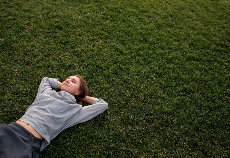 Person lying on grass practicing grounding techniques to feel calm and present