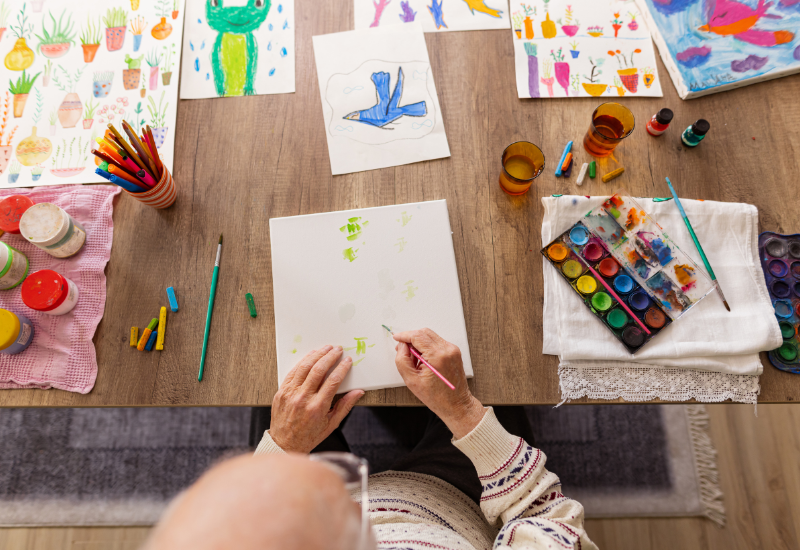 Benefits of art therapy shown through hands creating artwork with paints, crayons, and drawings on a table